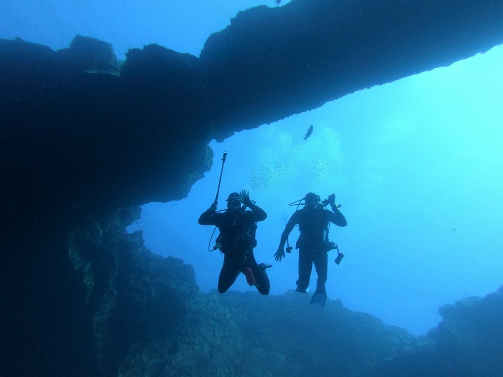 two divers pose for the camera underneath an underwater rock arch